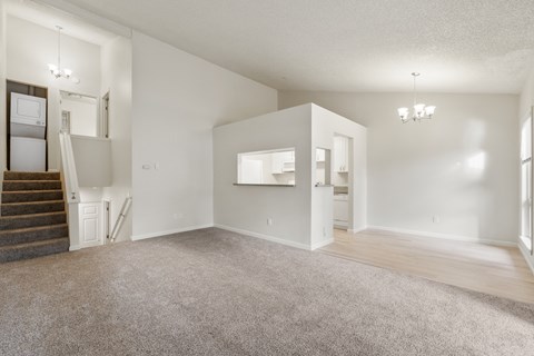 the living room of an apartment with carpet and a staircase