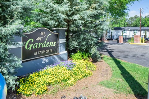 A sign for The Gardens at Camp Creek surrounded by flowers and trees.